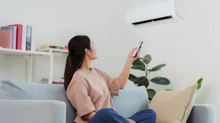 Femme assise sur un canapé utilisant une télécommande pour contrôler sa thermopompe murale
