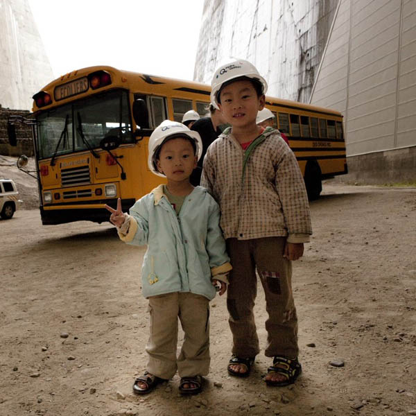 Children in front of a schoolbus under one of the arches of Daniel-Johnson dam.